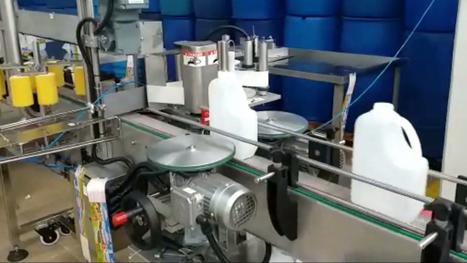 DDI four-side labeler applying labels to gallon jugs on a conveyor
