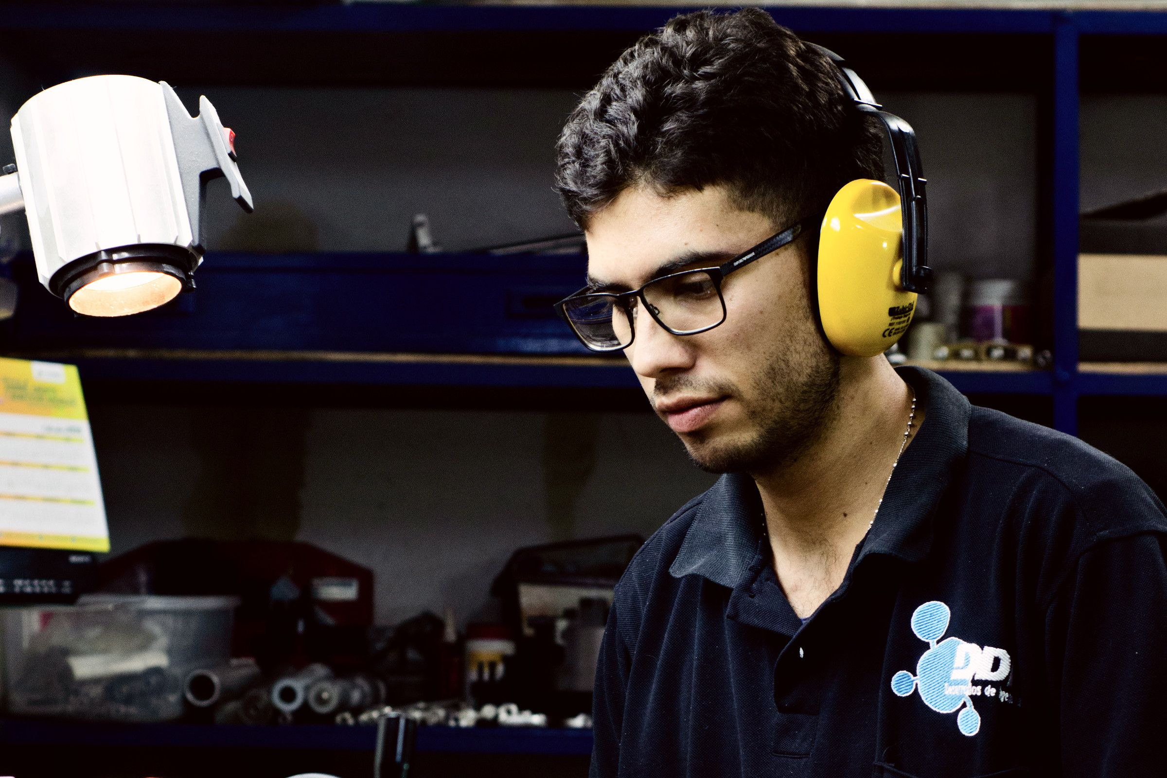 Técnico de DDI con protección auditiva operando un taladro en el taller.